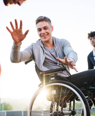 A boy in wheelchair with two teenager friends playing basketball outside at sunset.
