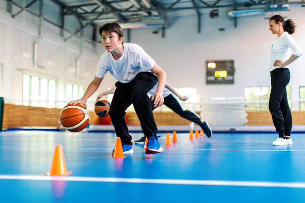 Studenten en hun coach basketten tijdens de turnles op school en de lerares kijkt toe.