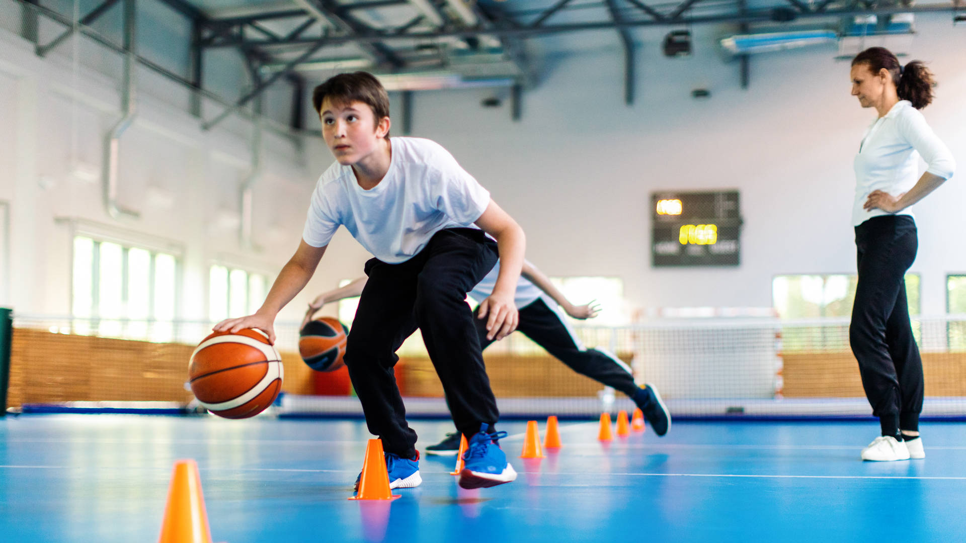 Studenten en hun coach basketten tijdens de turnles op school en de lerares kijkt toe.