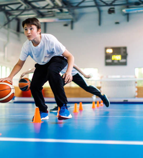 Studenten en hun coach basketten tijdens de turnles op school en de lerares kijkt toe.