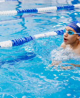 jongen zwemt met zwembril en badmuts in zwembad