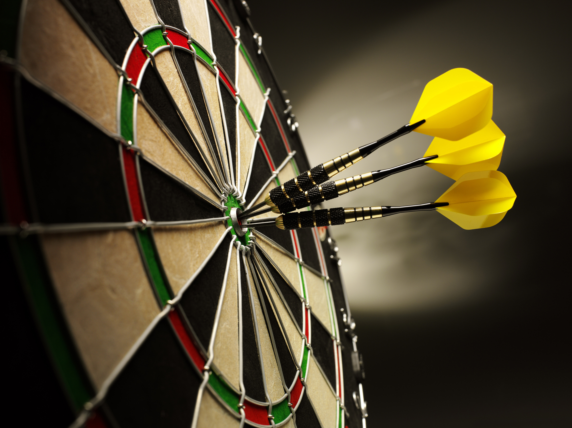 Three yellow darts hitting the target in a game of darts scoring a bulls eye.