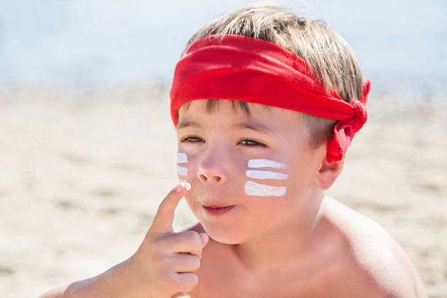 Who am I? Sunscreen (suntan lotion) is on hipster boy face before tanning during summer holiday on beach. Caucasian child (kid) is smiling in sunny day (not far from Trieste, Italy). Copy space.