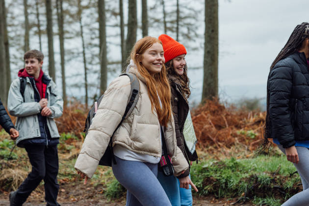 Side view three quarter length in Rothbury's woodlands, a group of student teenagers are on an educational walk. They explore nature, blending lessons with the outdoors.