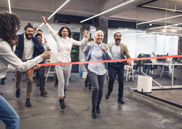 Large group of happy business people having fun while having a race at casual office. Focus is on mature woman.