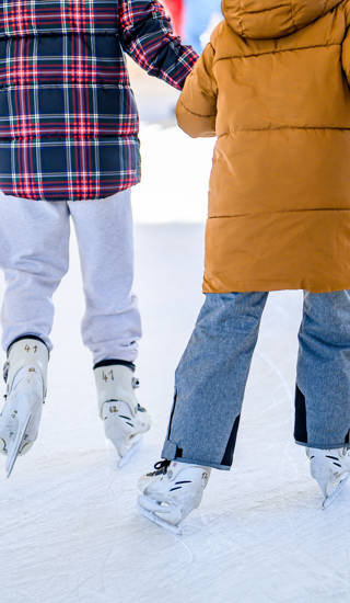 Two girls ice skating together and holding hands.