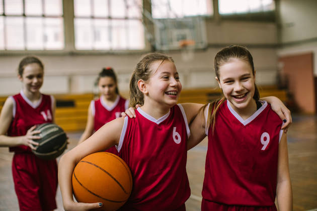 Jonge meisjes lachen en knuffelen elkaar na een basketbalmatch