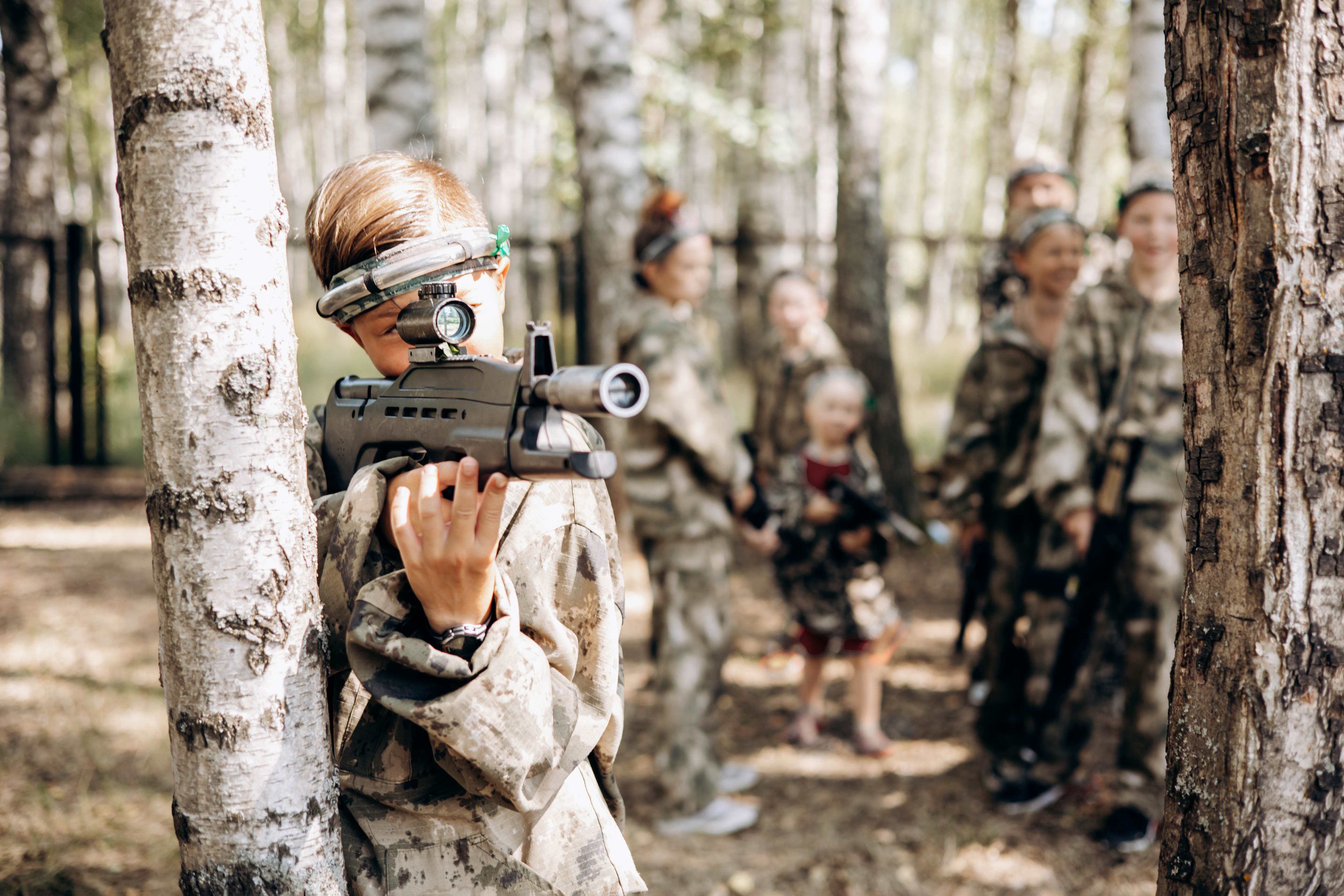 Boy looking into the optical sight a weapon. Children playing laser tag shooting game in outdoor. War simulation game