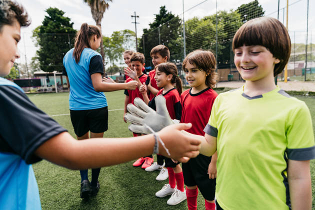Soccer kids players greeting each other in a row before a competition. Red and blue uniforms.