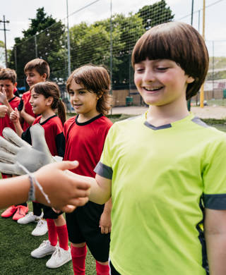 Soccer kids players greeting each other in a row before a competition. Red and blue uniforms.