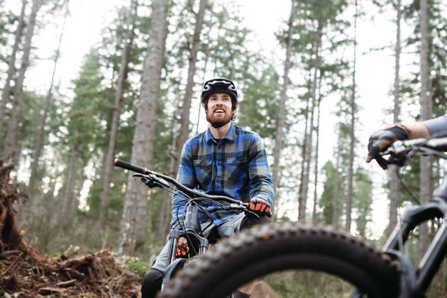 An adult man takes a break from a forest trail ride on his mountain bike, talking with a friend. Fun and healthy lifestyle image of recreational outdoor activity.