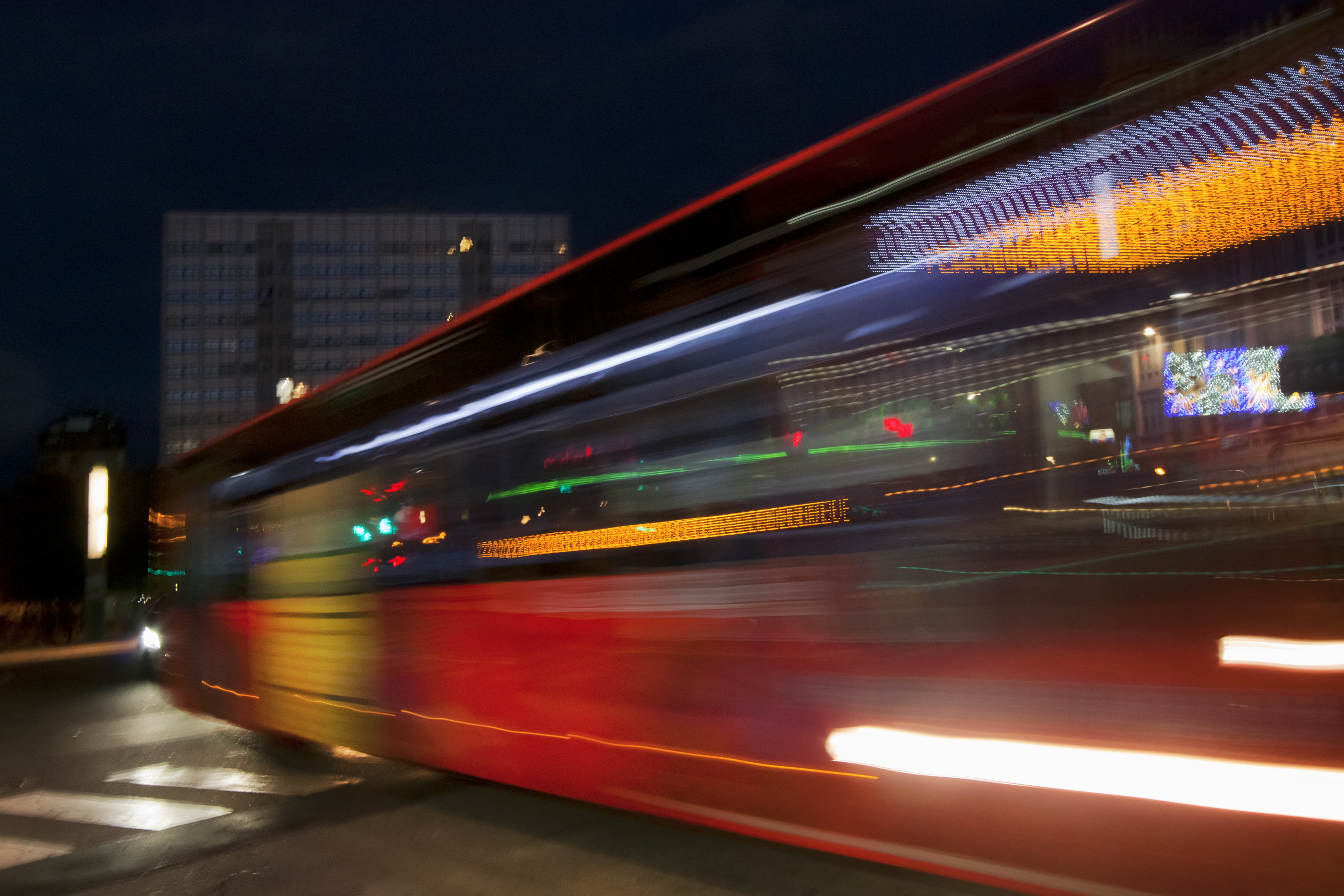 Traffic, bus moving fast in the foreground at night, building in the background.
A CoruÃ±a, Galicia, Spain.