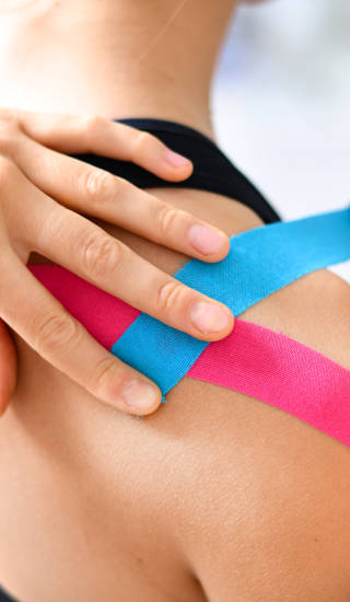 Kinesiology taping treatment with blue and pink tape on athlete patient injured arm. Woman hands apply kinesio treatment after sports muscle injury.