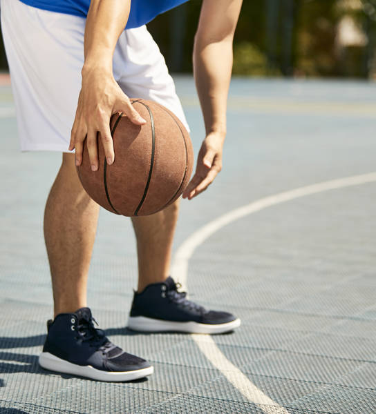 jonge basketter dribbelt met bal, enkel benen zichtbaar