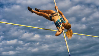 Vrouw springt over lat met polsstok