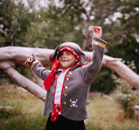 Excited little Boy dressed up as pirate grinning with toothy smile and missing some teeth. Fallen tree and log in the nature background