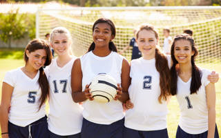 Members Of Female High School Soccer Team Smiling To Camera