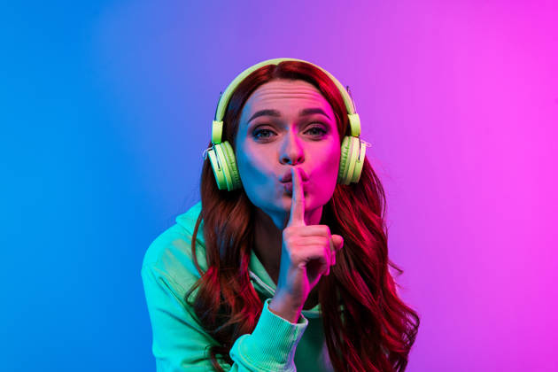 Photo of charming positive woman wear green sweatshirt headphones enjoy songs asking keep silence isolated neon blue color background.