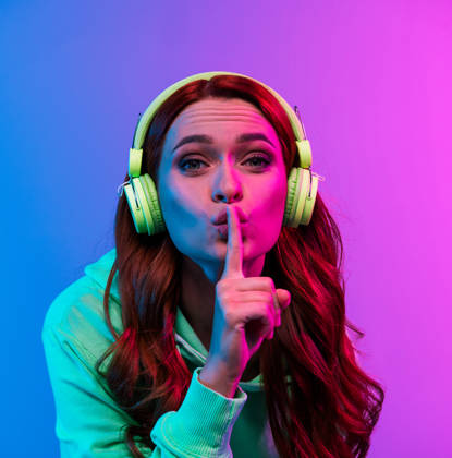 Photo of charming positive woman wear green sweatshirt headphones enjoy songs asking keep silence isolated neon blue color background.