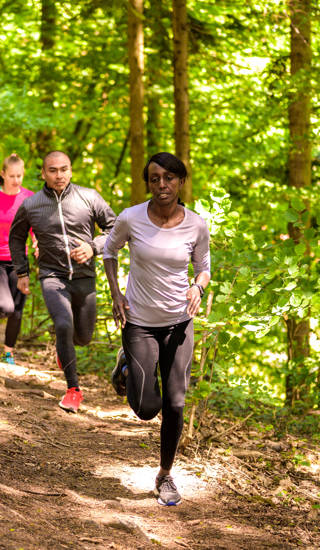 Front view of man and women running on footpath in forest.