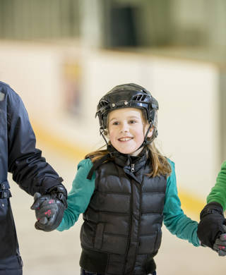 A mother is ice skating with her two daughters. They are holding hands and smiling.