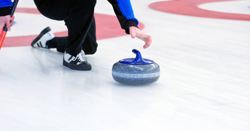 Curling speler schuift steen over ijs