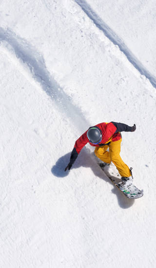 man op snowboard met bruine broek en rode jas