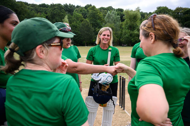 Women and Girls cricket teams playing a match on a sunny day outdoors on grass pitch