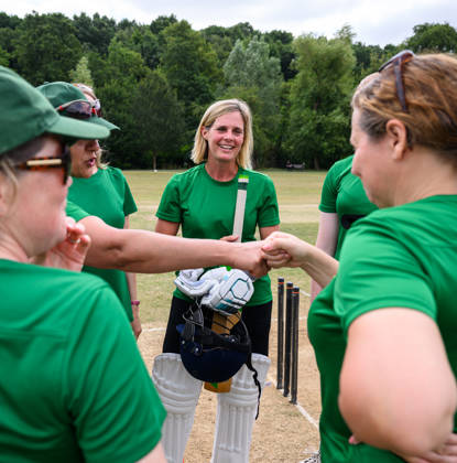 Women and Girls cricket teams playing a match on a sunny day outdoors on grass pitch