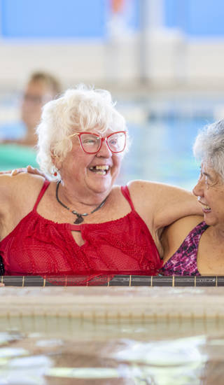 A group of happy seniors taking a water aerobics class at a community centre. The women use various pool equipment to exercise.