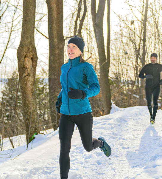 A mature couple in the winter running together in nature