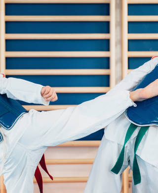 Twee personen in kimono met blauw vestje, de ene met voet tegen borst van de andere