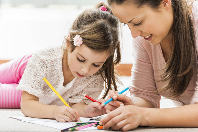 Young mother drawing with her little daughter while lying down on carpet at home.
