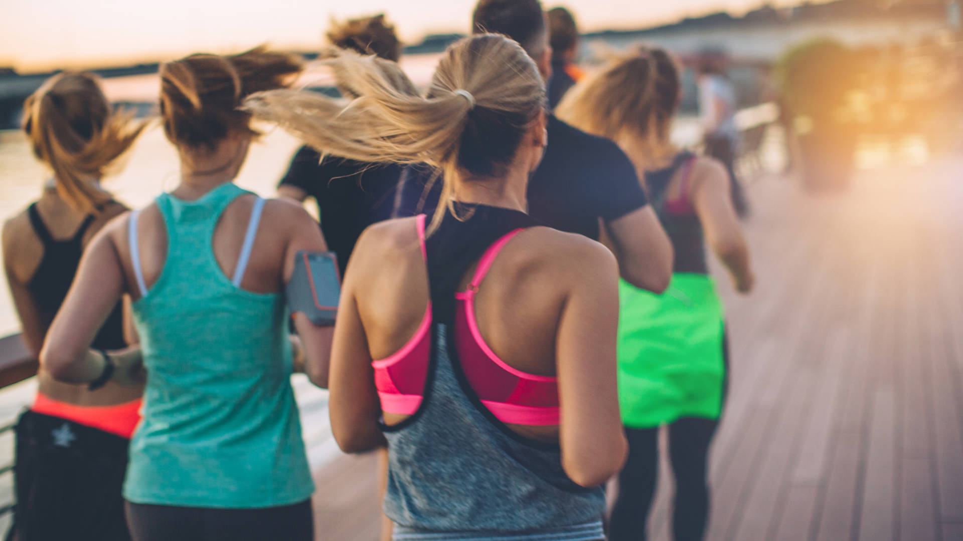 Group of young people competing in a race. Young men and women on riverside promenade running. They are wearing sport clothing. View from behind.
