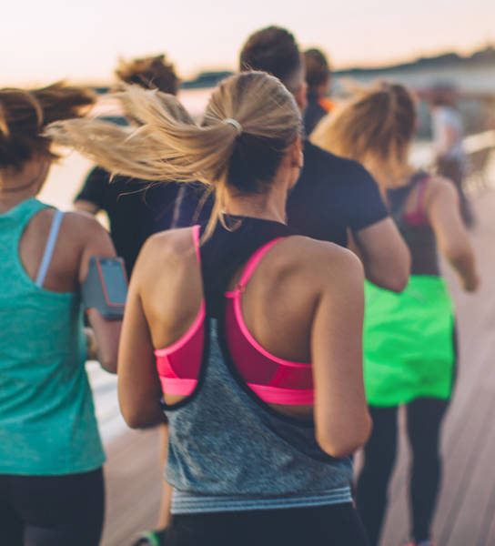 Group of young people competing in a race. Young men and women on riverside promenade running. They are wearing sport clothing. View from behind.