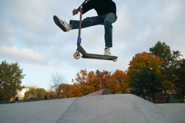 Teenager performs trick in the city skate park. Push scooter. He is jumping. Extreme sports is popular among youth. View of park of body