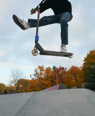 Teenager performs trick in the city skate park. Push scooter. He is jumping. Extreme sports is popular among youth. View of park of body