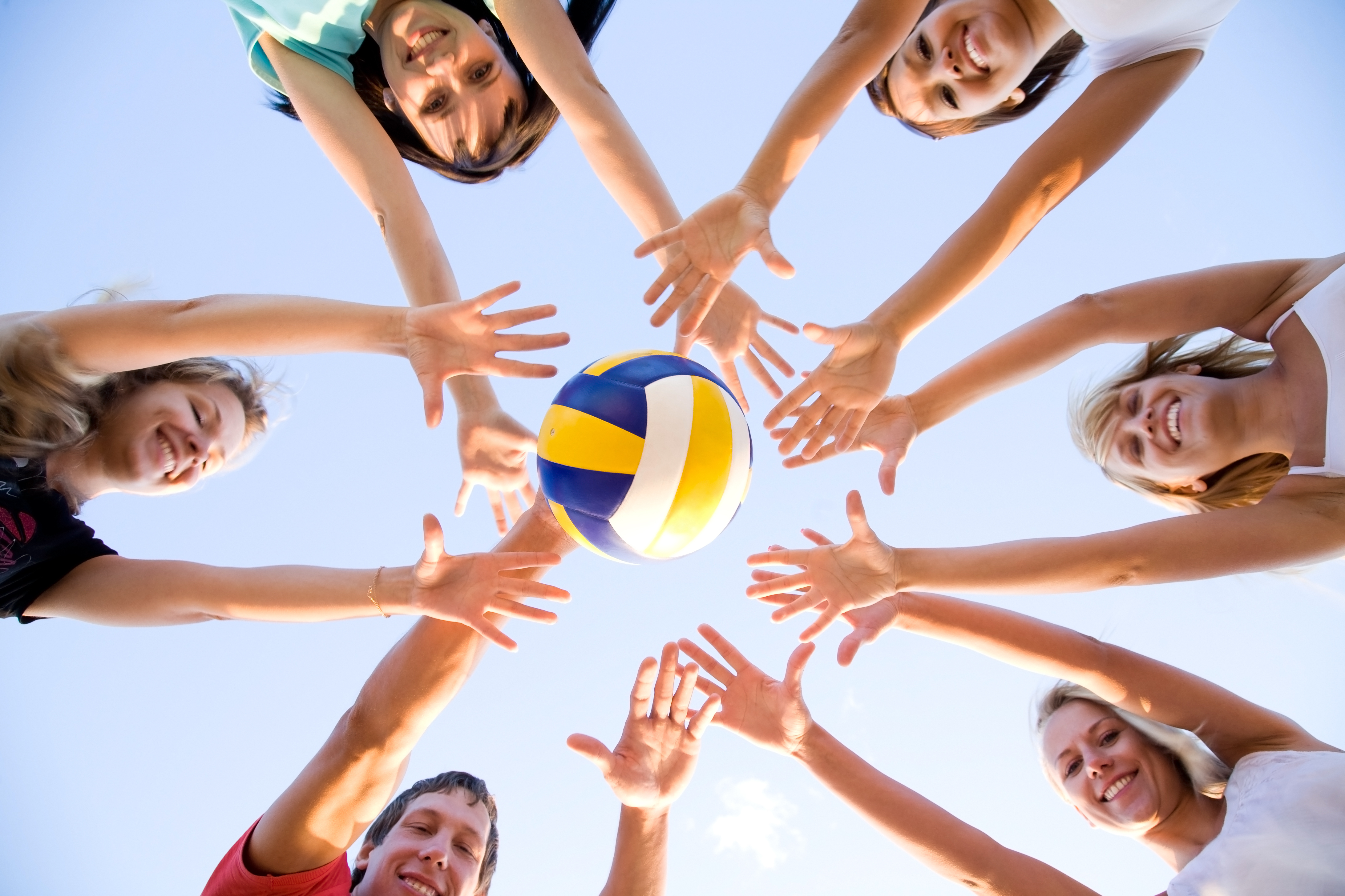 Groep steekt handen in de lucht met volleybal in het midden