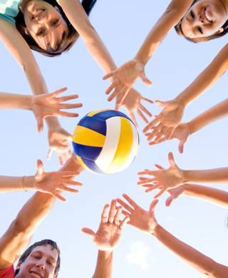 Groep steekt handen in de lucht met volleybal in het midden