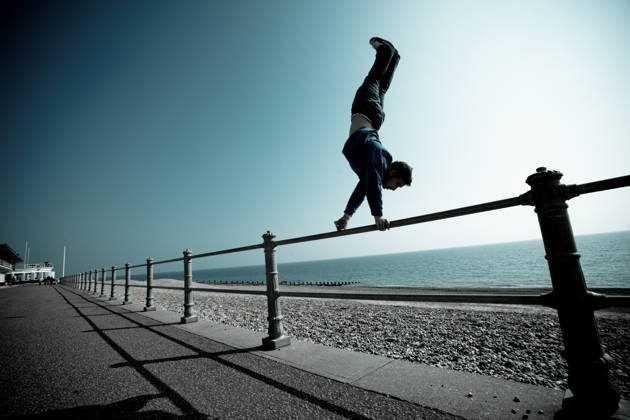 Man doet handstand op omheining aan zee