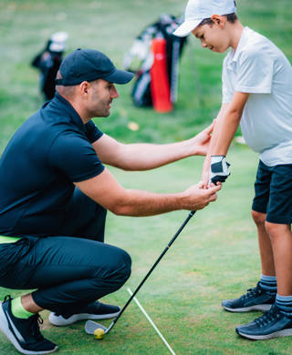 Golf coach helpt jongen om stick goed vast te houden