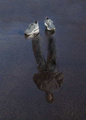 Lege sportschoenen staan in plas water. In het water zie je de reflectie van een jonge man in sportkledij