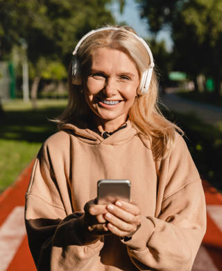 Cheerful sporty slim mature woman female runner athlete choosing sound track on smart phone while listening to the music radio podcast while training jogging in stadium