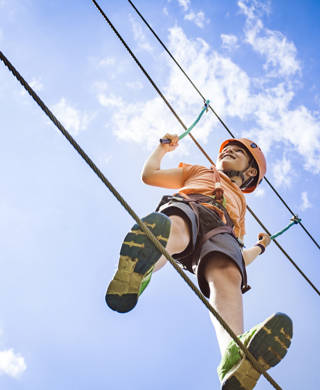 Boy at the adventure park walking on a rope high up in the air.