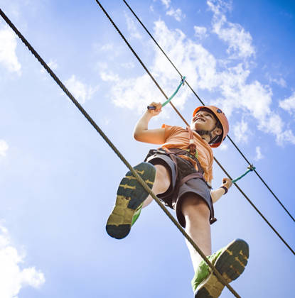 Boy at the adventure park walking on a rope high up in the air.