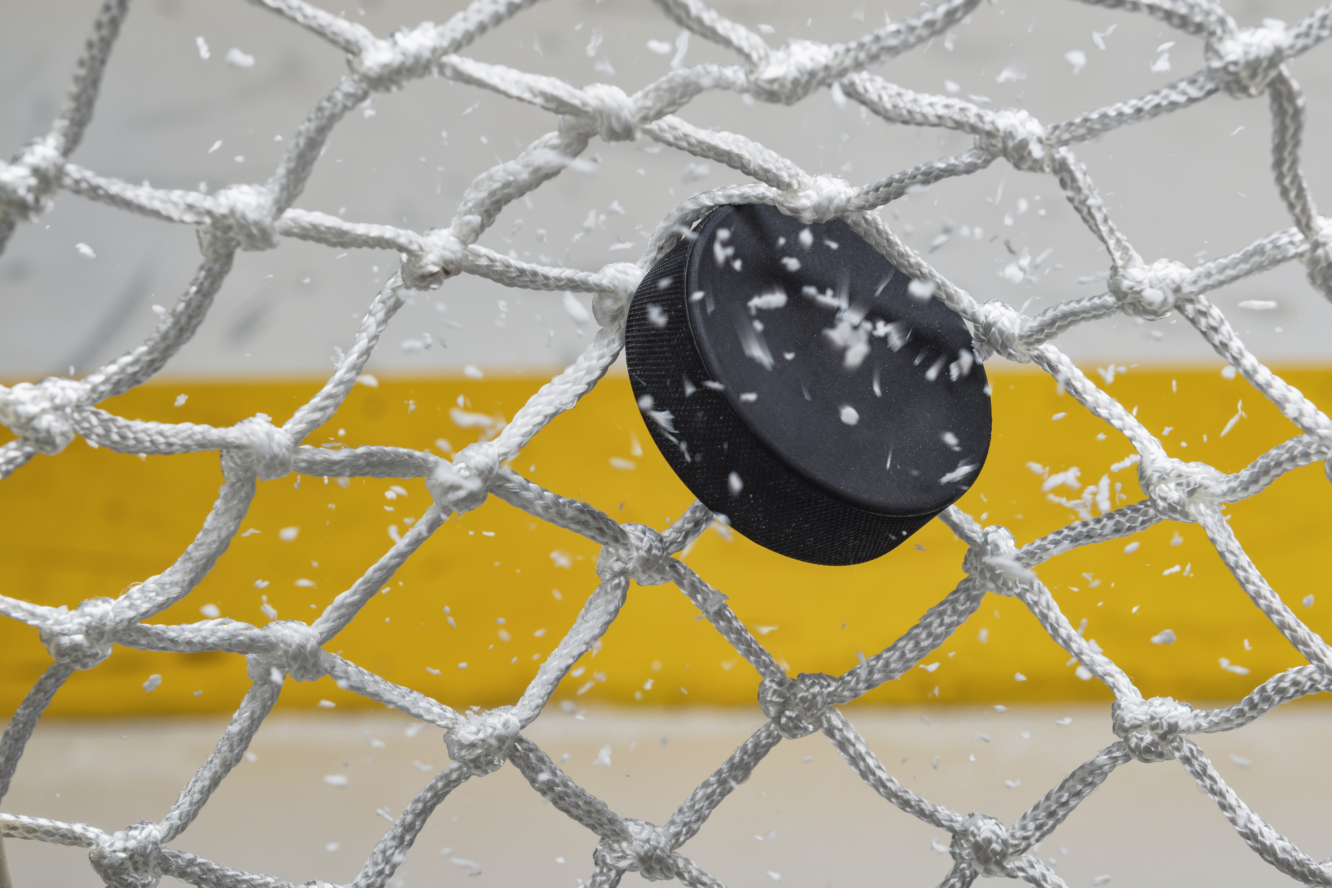 A close-up view of an Ice Hockey puck hitting the back of the goal net as shavings fly by, viewed from the front. Scoring a goal in ice hockey.