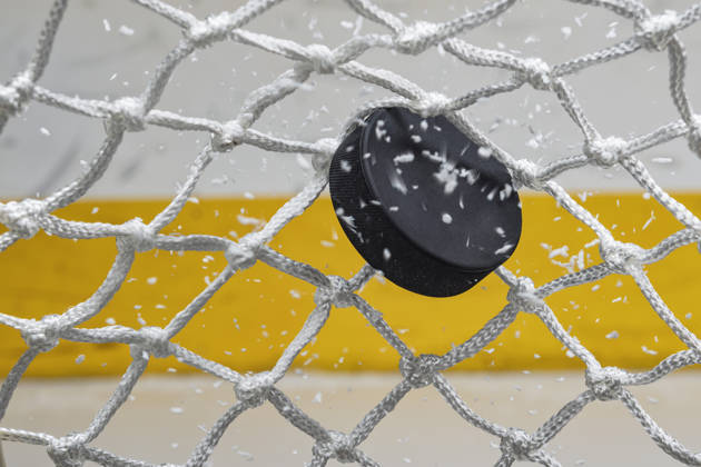 A close-up view of an Ice Hockey puck hitting the back of the goal net as shavings fly by, viewed from the front. Scoring a goal in ice hockey.