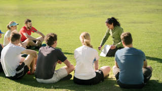 Shot of football players sitting in front of coach on football field listening to pre game speech