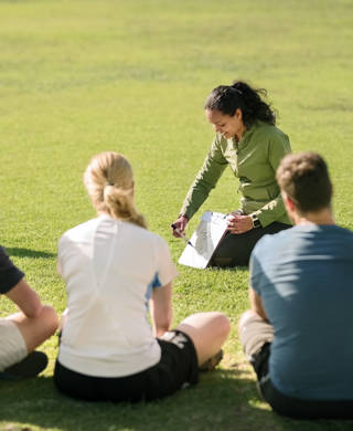 Shot of football players sitting in front of coach on football field listening to pre game speech