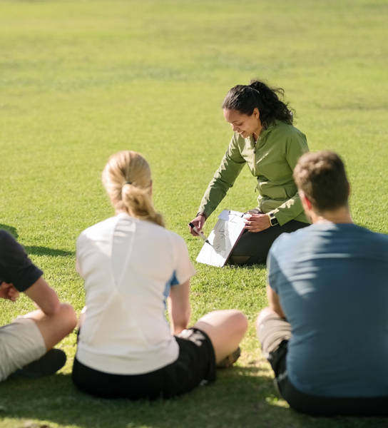 Shot of football players sitting in front of coach on football field listening to pre game speech
